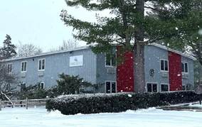 A building with a red door and a tree in the snow

Description automatically generated